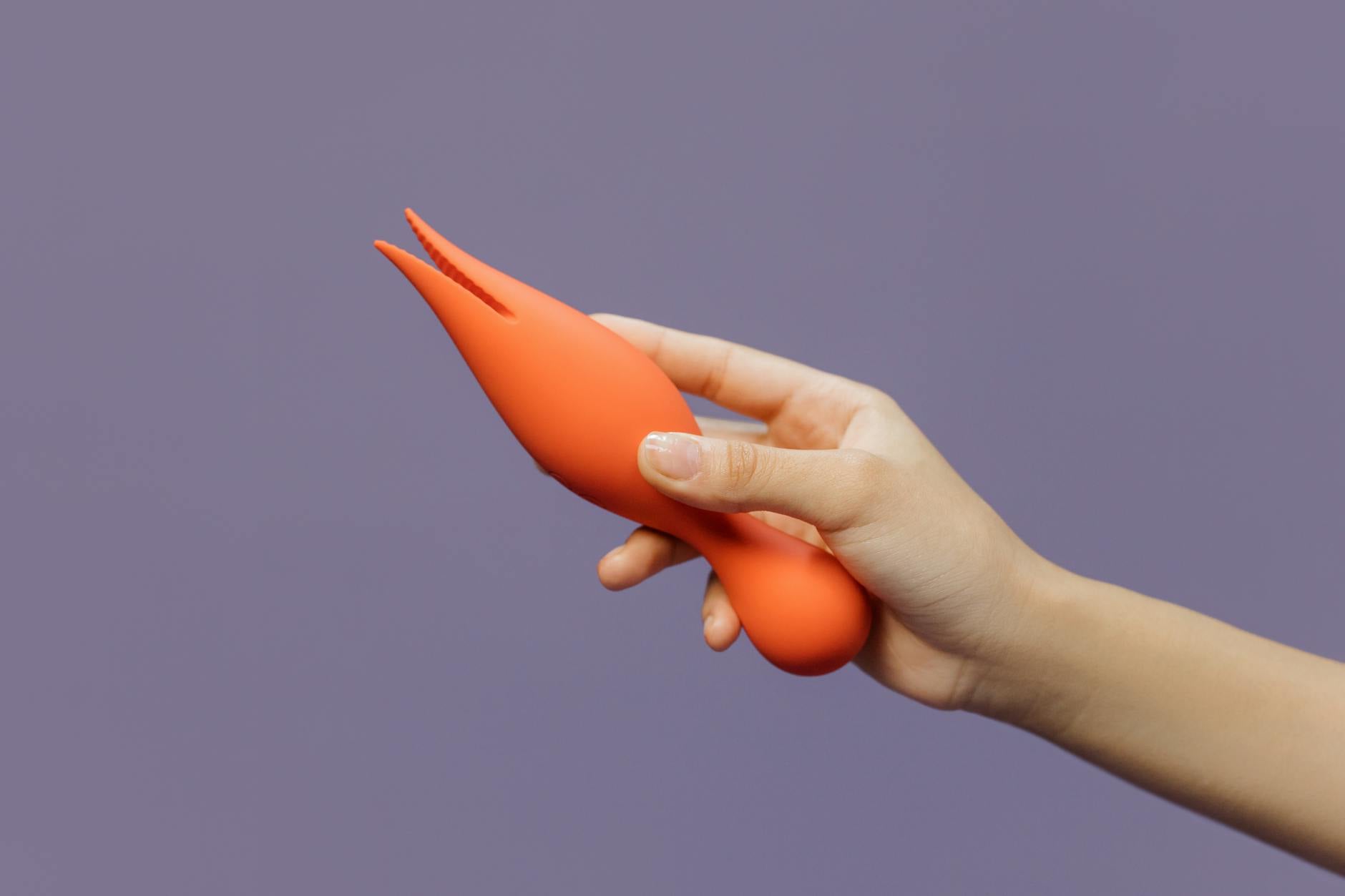 Hand holding an orange vibrator against purple backdrop, emphasizing intimate sensuality and self-care